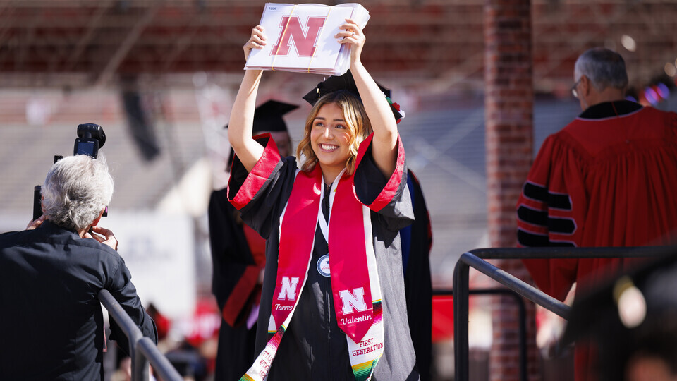 Graduate Monzeratt Valentin smiles as she holds her diploma above her head.