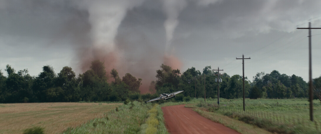 A fixed-wing drone flies toward storm clouds over a country road.