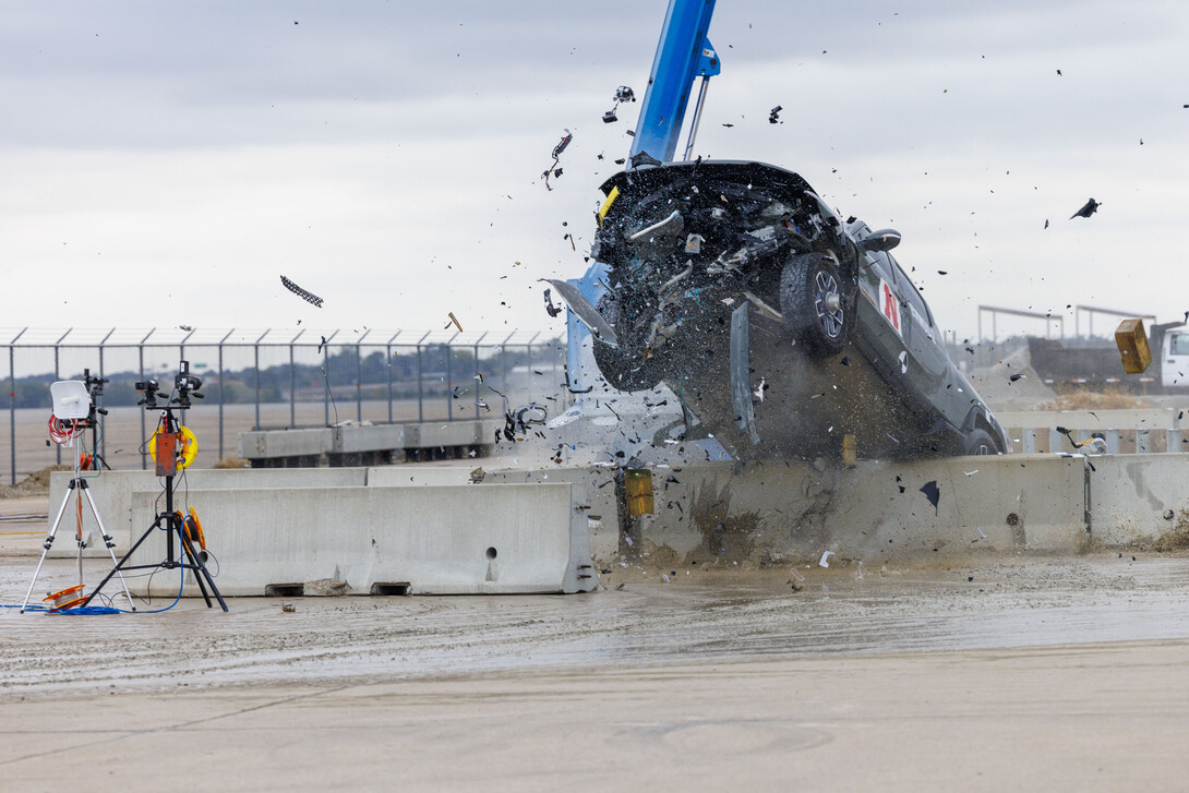 A Rivian pickup crashes over a concrete barrier.