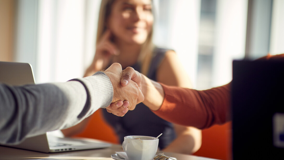 A man and woman shake hands as a woman smiles in the background.