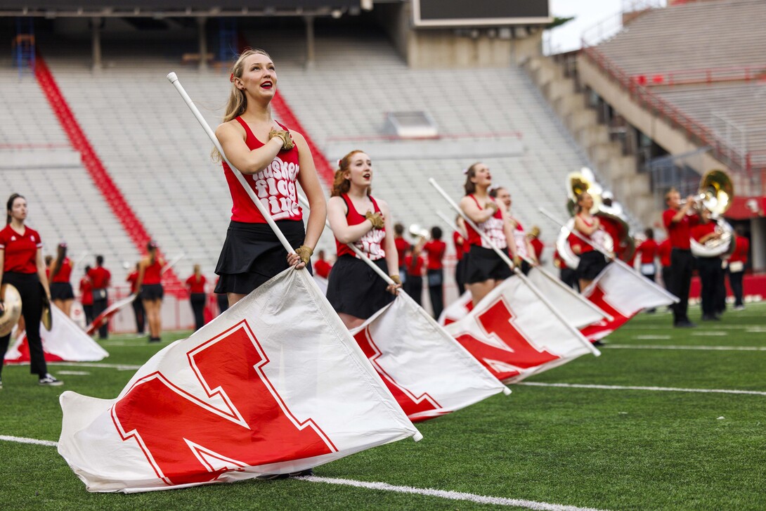 The Cornhusker Marching Bande flag line stands at attention on the field at Memorial Stadium.