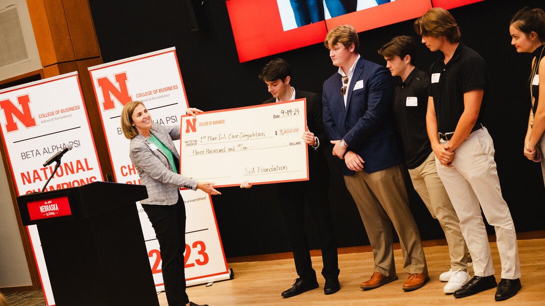 Jill Trucke, associate professor of practice in accountancy, awards a large $3,000 check to a Husker student, while four other students stand on stage.