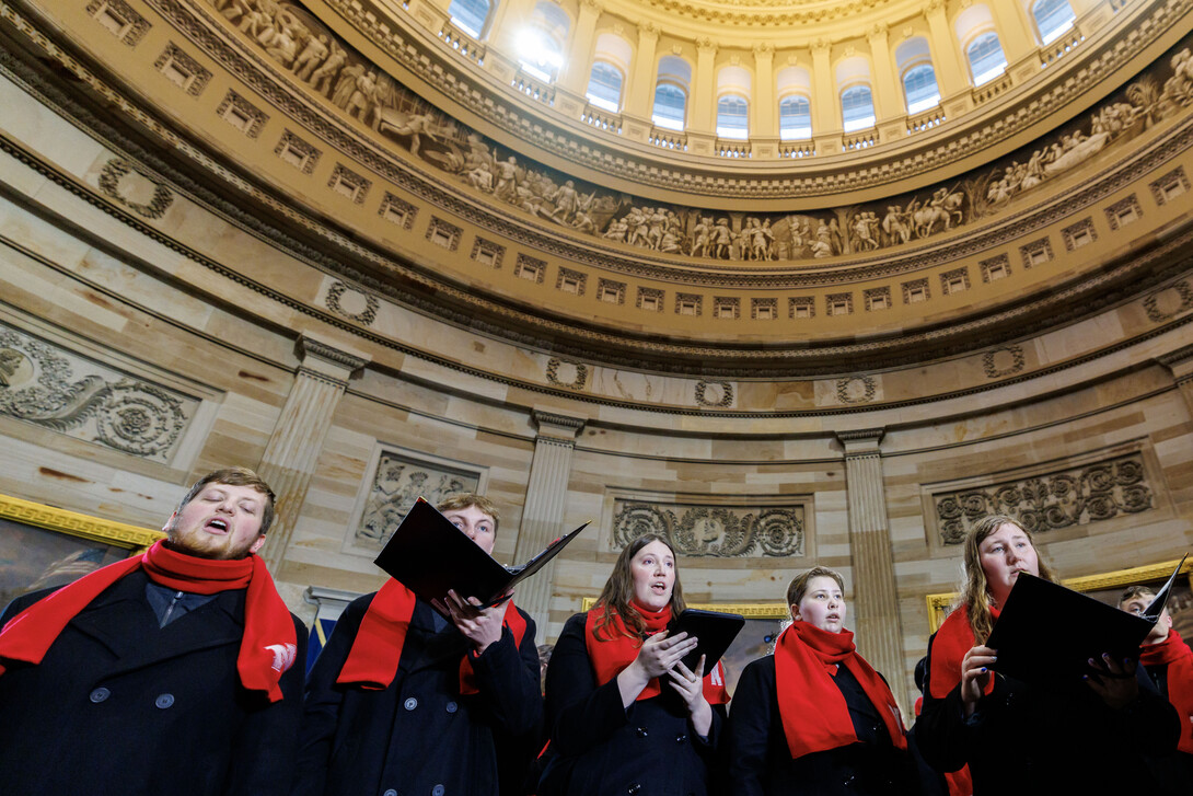 Six choirs members, dressed in black peacoats with red scarves, perform inside the U.S. Capitol.