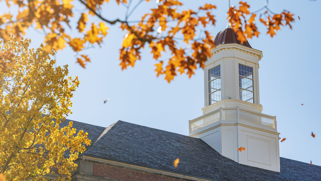 Branches full of yellow and orange fall leaves appear in front of the Love Library cupola.