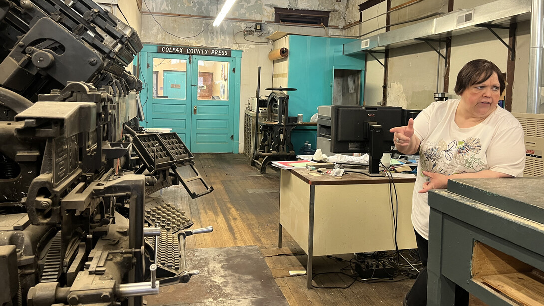 Tonya Evans, owner and publisher of the Colfax County Press in Clarkson, Nebraska, leans on a table across from an old printing press.