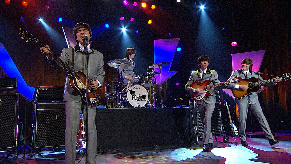 The Fab Four, in matching gray suits with mop-top haircuts, perform onstage as The Beatles.