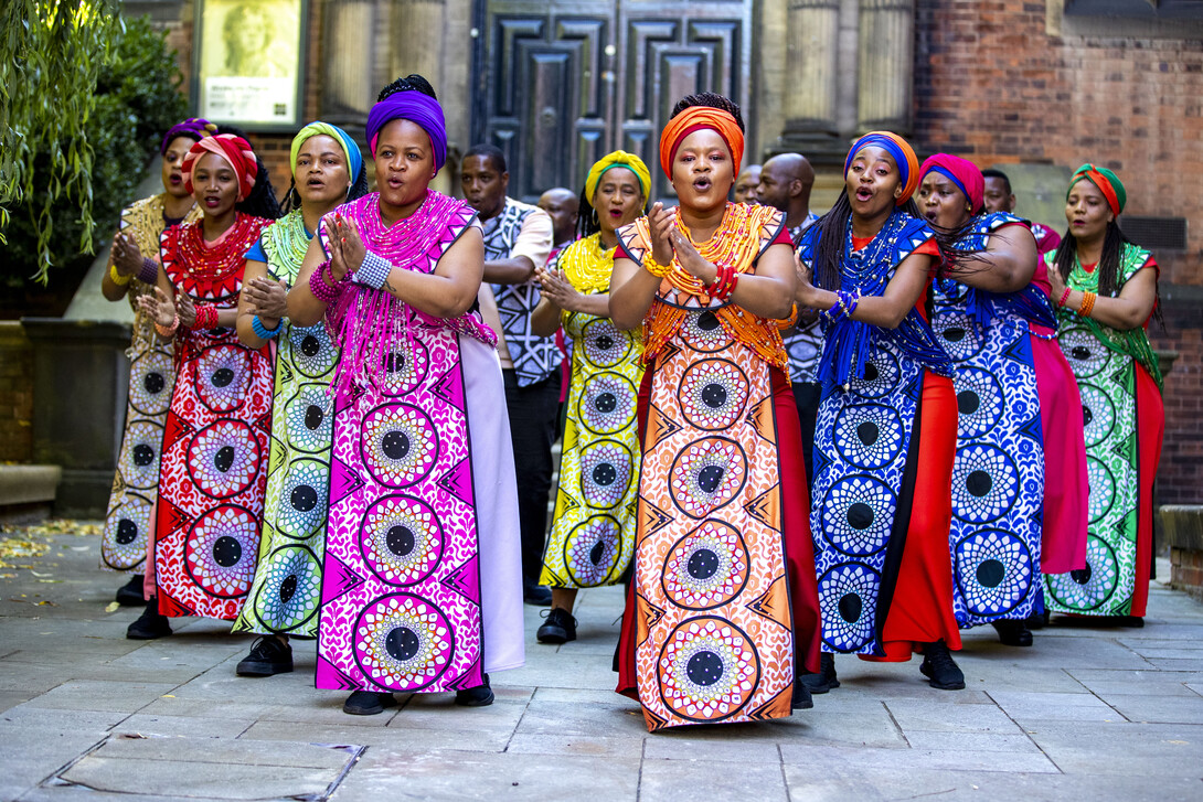 African-American women sing while wearing colorful dresses.
