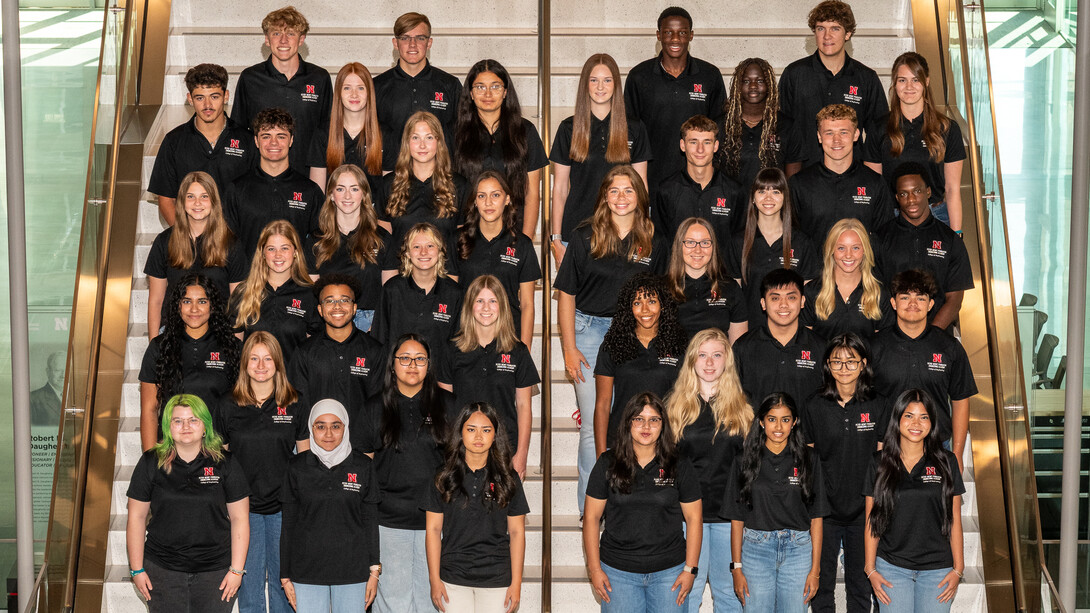 Forty Husker students in black polo shirts — all members of the 2025-26 cohort of the Peter Kiewit Foundation Engineering Academy — pose for a photograph on a staircase in Kiewit Hall.