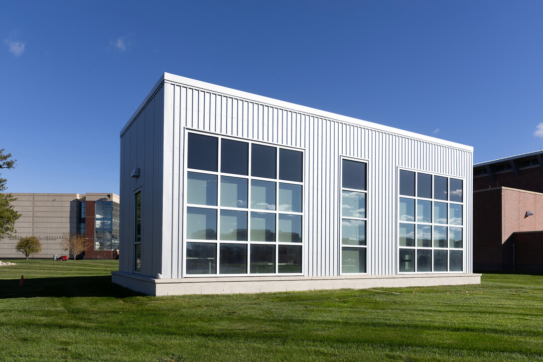 An exterior photo of the Human-centered Integrated Building Operations Laboratory at the Peter Kiewit Institute, a 1,000-square-foot rectangular building with gray siding and large windows.