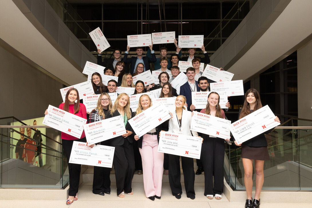 Twenty-six students — all winners in this year's 3-2-1 Quick Pitch competition — pose with oversized checks on a staircase in Howard L. Hawks Hall.
