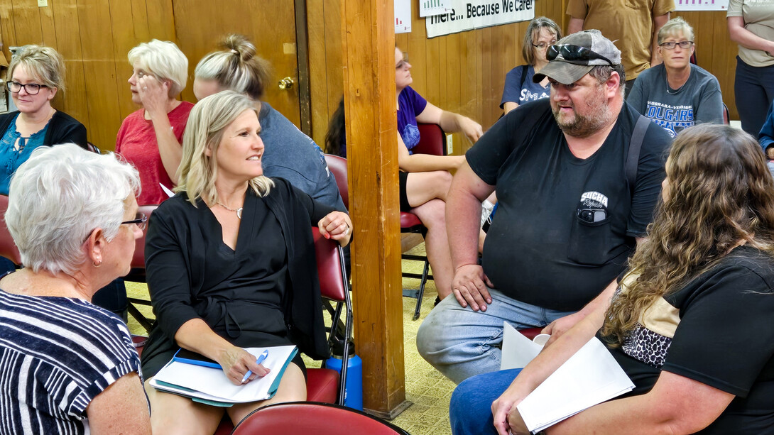 Three women and a man talk while seated in a circle, with other discussion circles in the background.