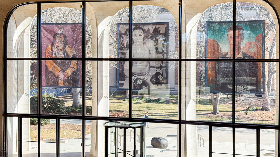 Three banners featuring people hang over the east windows of Sheldon Museum of Art.