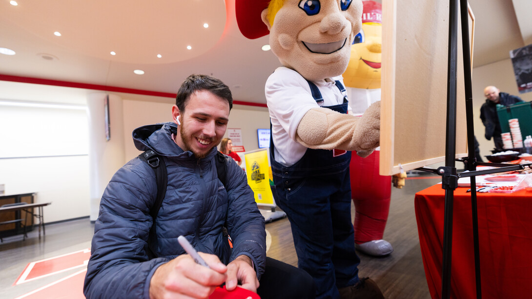 Zac Hartman, a junior mechanical engineering major, writes what he loves about the University of Nebraska–Lincoln on a heart for Glow Big Red. Next to Hartman are mascots Herbie Husker and Lil' Red