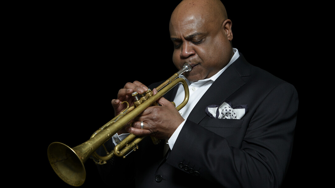 A man in formal attire plays a trumpet.