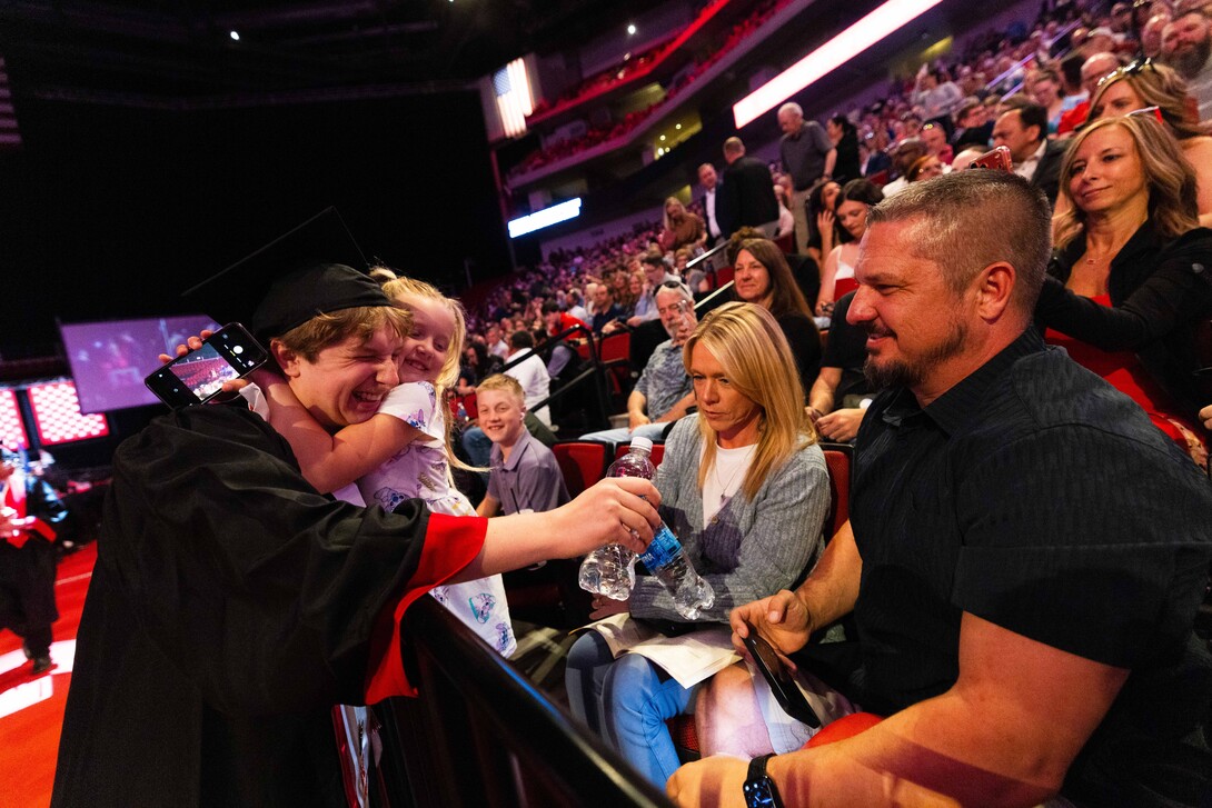 A male graduate receives a hug from his younger sister as he visits his family after receiving his diploma.
