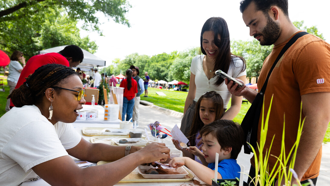 Bellodgia Roberson, a graduate student in agronomy, helps 3-year-old Jasper Molina make a soil profile during an East Campus Discovery Days event in June 2025. The boy's mother, father and sister watch.