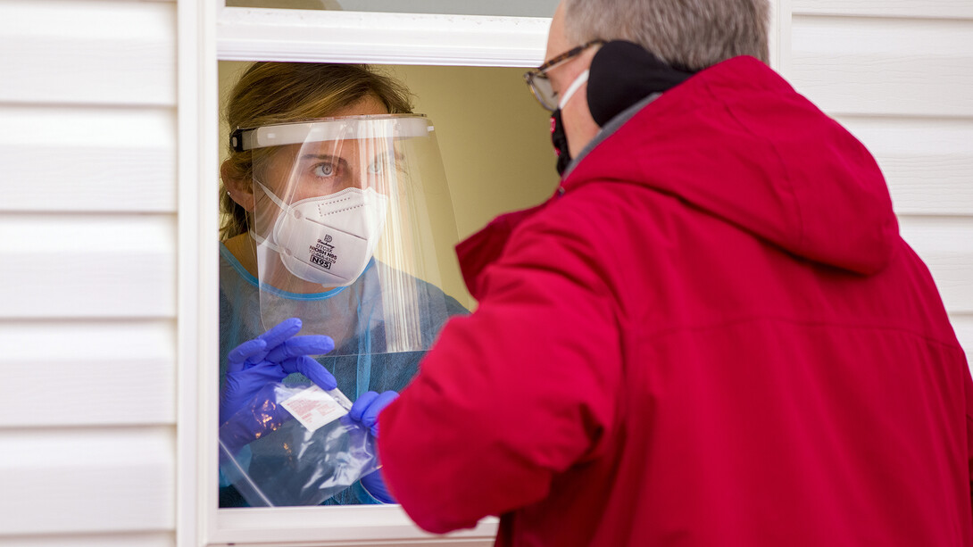 Bria Foley, a senior pre-med major, hands a package that contains a vial, straw and alcohol wipe to a walk-up test to a walk-up testee at the East Stadium COVID-19 saliva test station on Jan. 19.