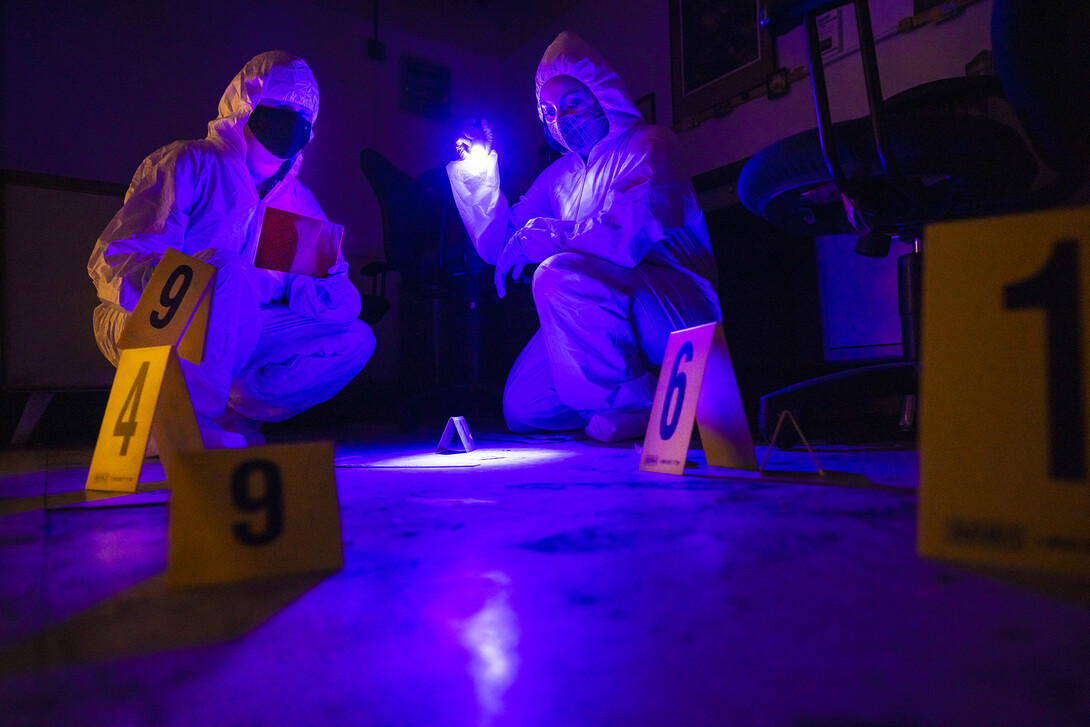 Symone Arends, a senior from Lincoln, shines an ultraviolet light onto the floor. The light will make body fluids and fibers  glow when viewed through the filter held by Alysa Ehlers, a senior from Woodbridge, Virginia. The two are working a mock crime scene in a basement room in Filley Hall.