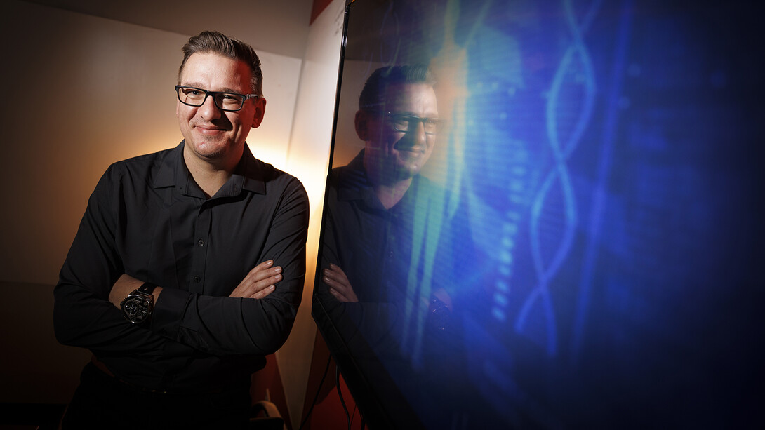 Tomas Helikar standing in front of a television screen which has two DNA strands in blue.