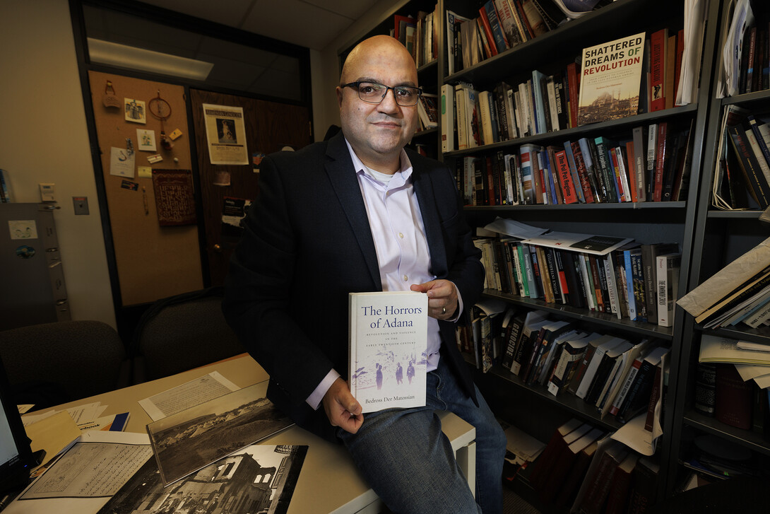 Bedross Der Matossian is photographed near his office book shelf, holding a copy of his new book, "The Horrors of Adana."