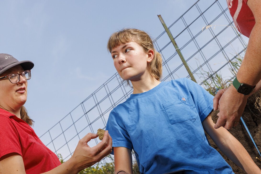 Kennadi Griffis listens to Judith Turk, one of her coaches,  as they discuss a soil sample in the pit on East Campus.