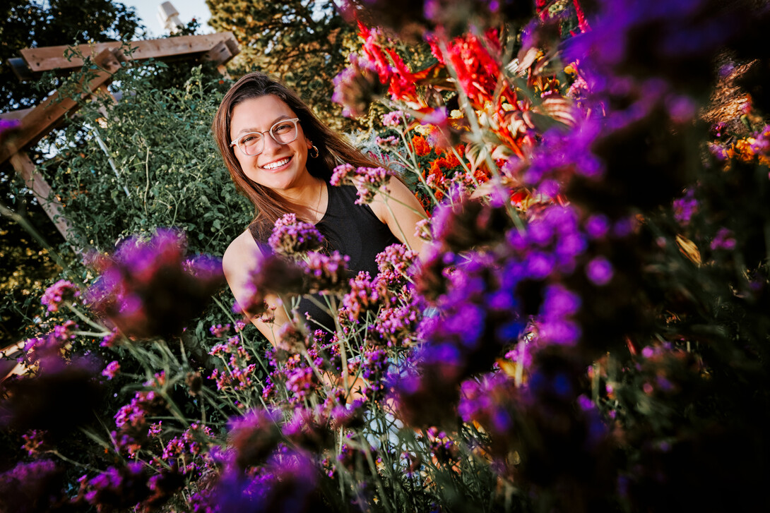 Isabella smiles for a photo surrounded by flowers on East Campus