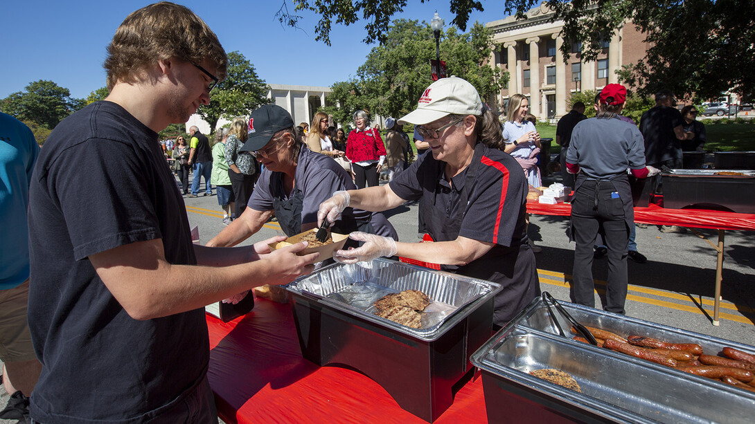 Claudia Wheeler, a dining services clerical associate, serves a hamburger to Raymond Guern, a production technician with the Lied Center for Performing Arts, during the picnic. Dining Services workers from across campus volunteered to work the event.