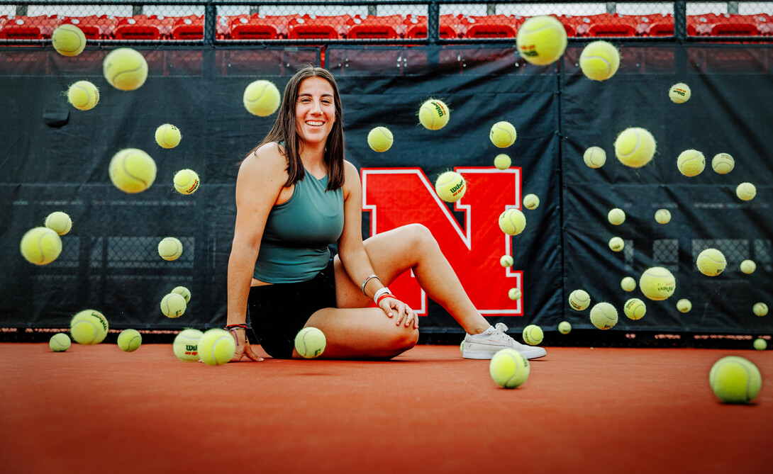 Tennis balls bounce around Isabel as she sits for a photo on the tennis court.