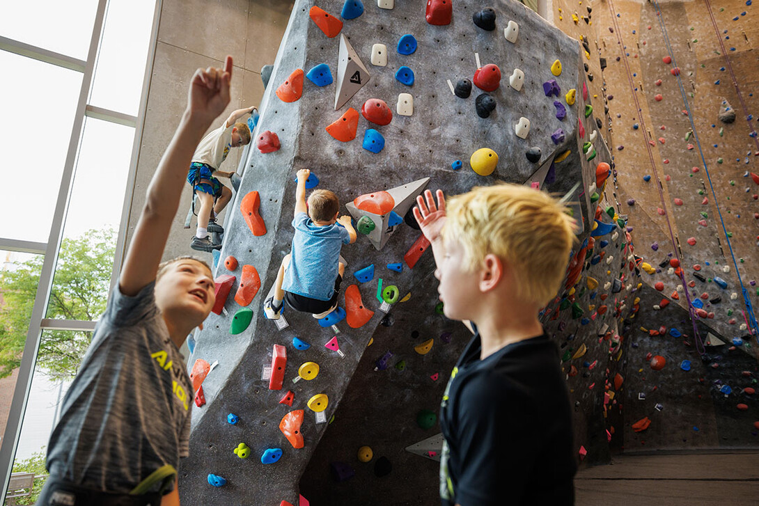 Campers discuss their strategy in front of the rock climbing wall as others take on the climbing the wall.