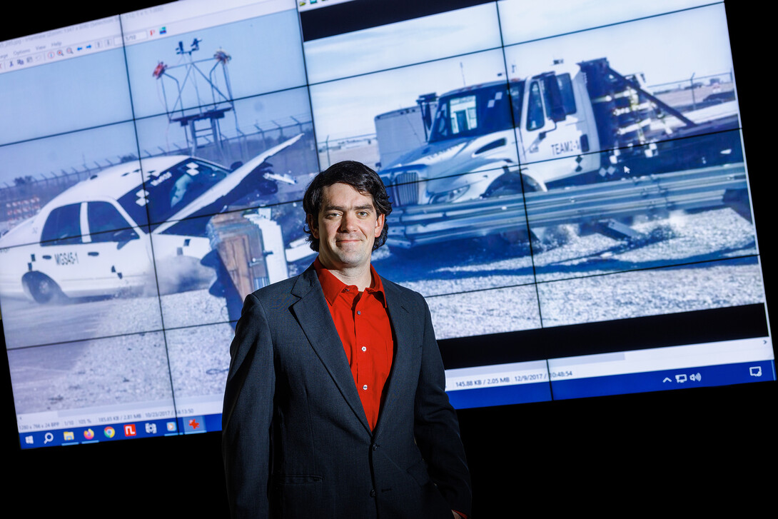 Cody Stolle posed in front of crash video footage from testing done at the UNL Midwest Roadside Safety Facility.