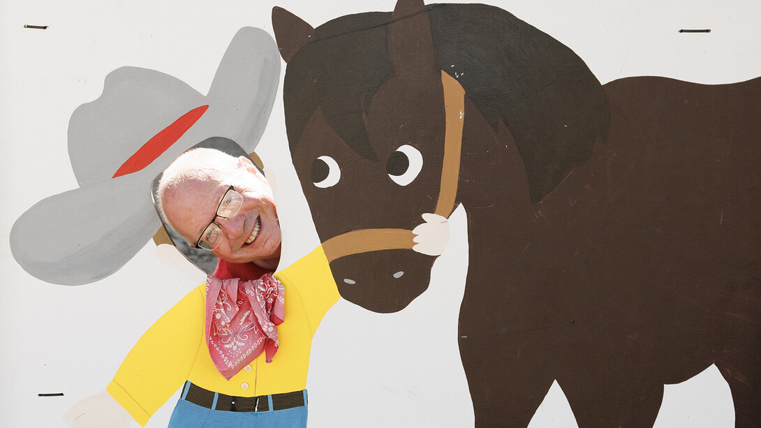 Craig Chandler pokes his head through a hole in a painted board, looking like a cowboy getting ready to ride a horse, while at the Gage County Fair in summer 2024.