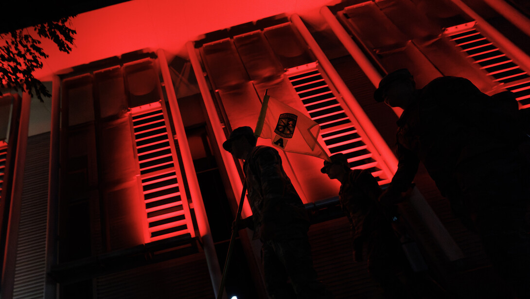 Army ROTC cadets carry their guidon past the red-lighted Schorr Center as they head into the stadium.