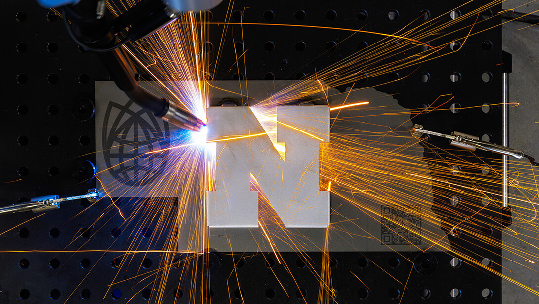 A robotic welder at Nebraska Innovation Studio welds a Nebraska N to a cutout in the shape of Nebraska.