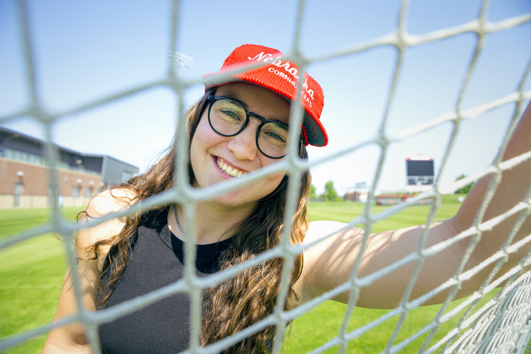 Photo by Kristen Labadie // Cece Villa, Husker soccer goalkeeper, smiles for a photo through the net of the goal.