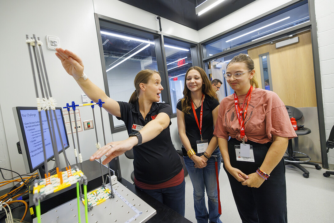 Christine Wittich, assistant professor in civil and environmental engineering, explains why the pointed top of the building designed by Moe McCall, center, and Bella Thomas did better than the building without a top.