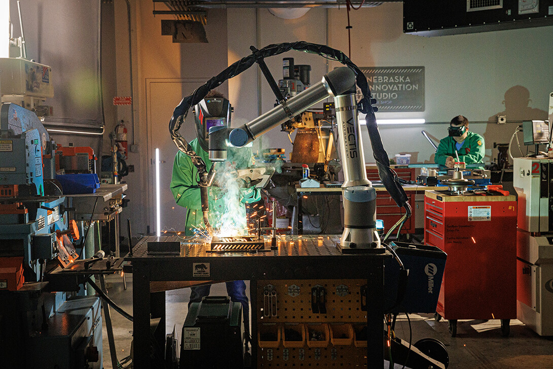 A Nebraska Innovation Studio member stands behind the welding robot, checking the programming on a tablet.