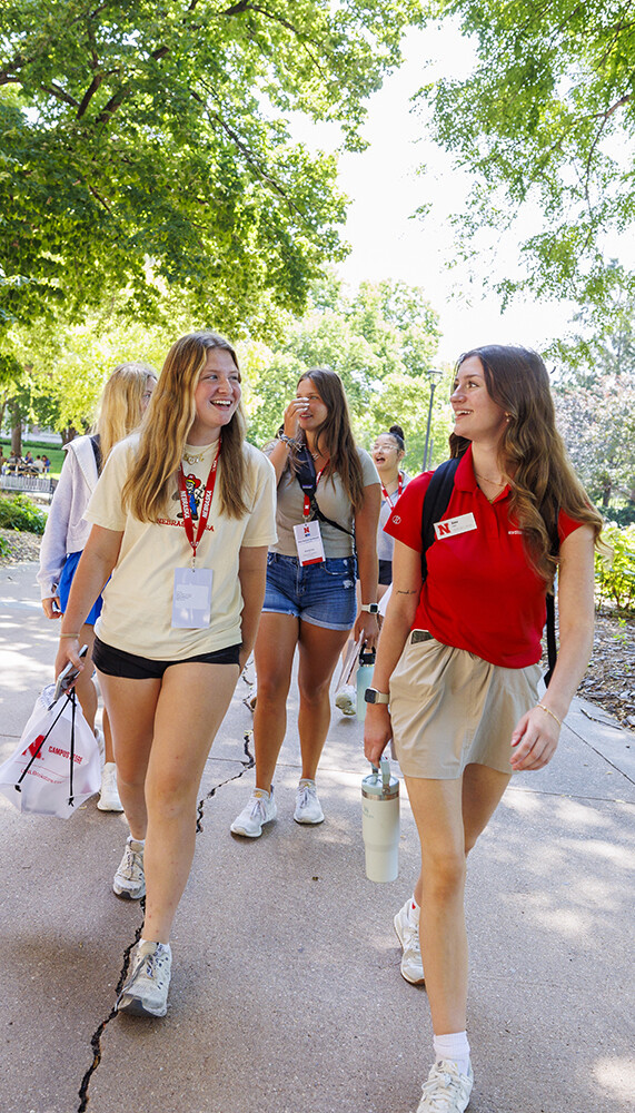 An NSE orientation leader chats with a student during a campus tour with trees in the background.