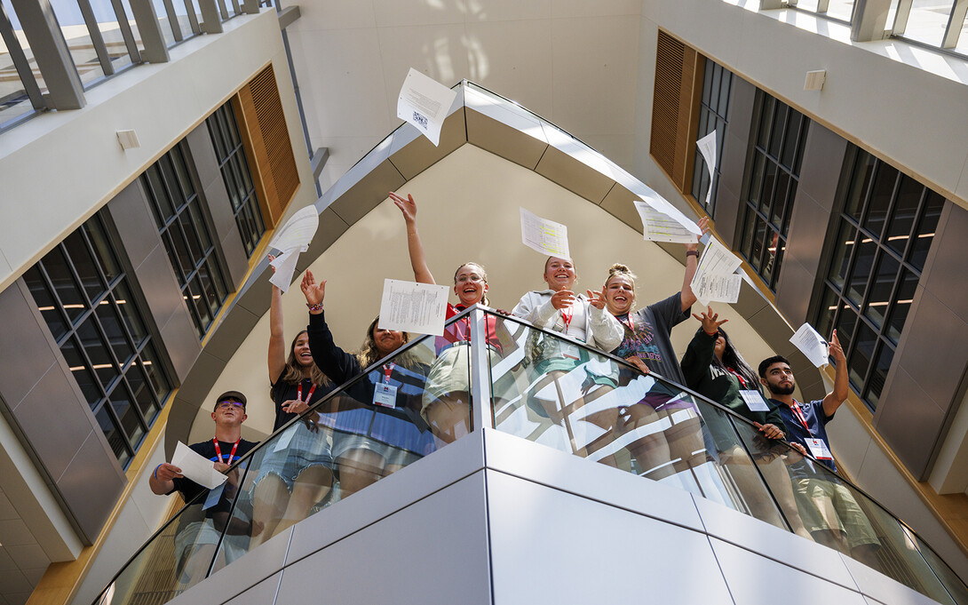 An NSE leader and student participants toss papers from a balcony in Hawks Hall.