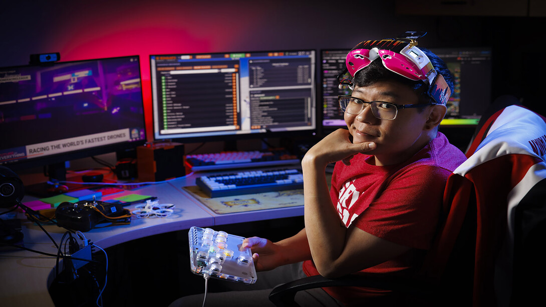 Ryan Tan sits in front of his desk of monitors displaying his research.