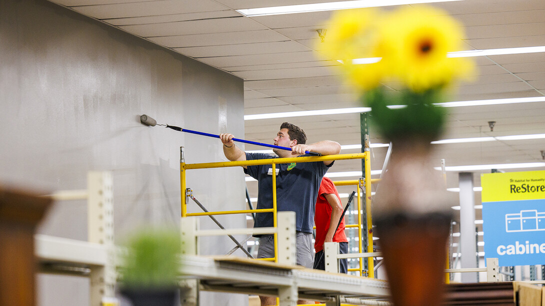 Framed by accent pieces in the store, Grant Guebbels paints the top of a wall using a scaffold.