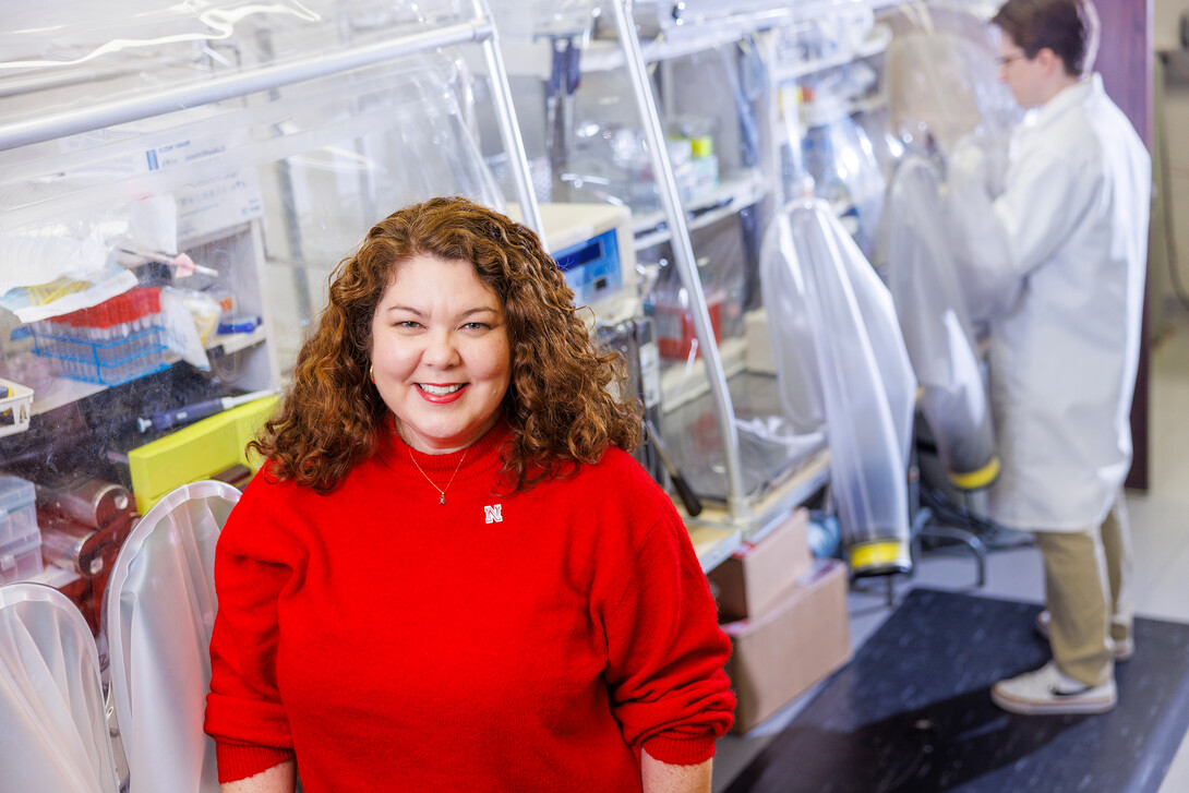 Dr. Nicole Buan sits on the left side of the frame in a red sweater, in front of a lab.