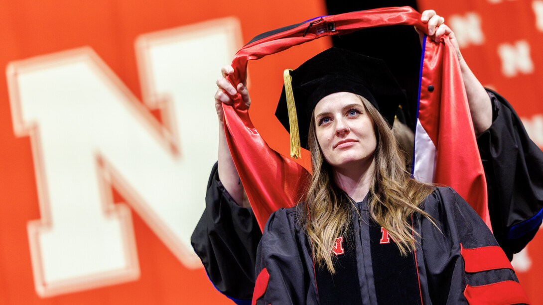 Nicole Fiore glances at the Pinnacle Bank Arena screen while being hooded during the graduate and professional commencement ceremony on Dec. 20, 2024. Spring 2025 commencement exercises will be May 3 for the College of Law, May 16 for graduate and professional degrees, and May 17 for undergraduates.