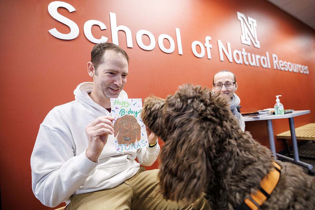 Kenneth Pyle, left, student success coach in the School of Natural Resources, shows his dog Jonas a birthday card during Jonas’ fourth birthday party inside Hardin Hall Feb. 20.