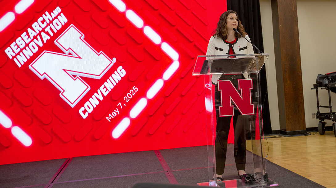 Jen Nelson, interim vice chancellor for research and innovation, stands at a podium in front of a red screen that says "Research and Innovation Convening" with the iconic Nebraska N.
