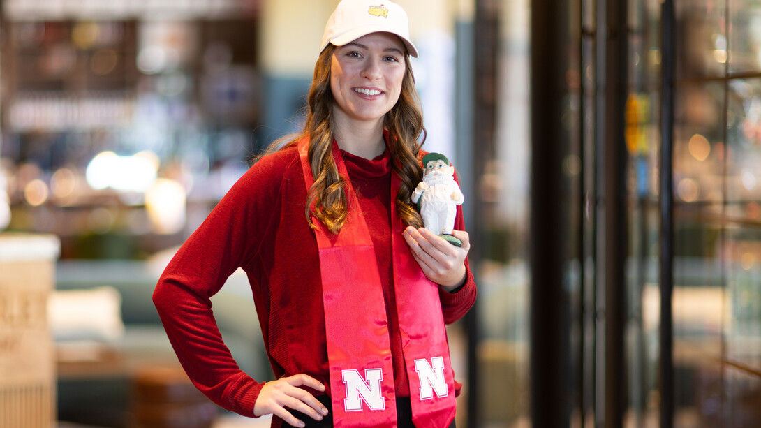 A woman wearing a cap and graduation sash holds a figure and faces the camera.
