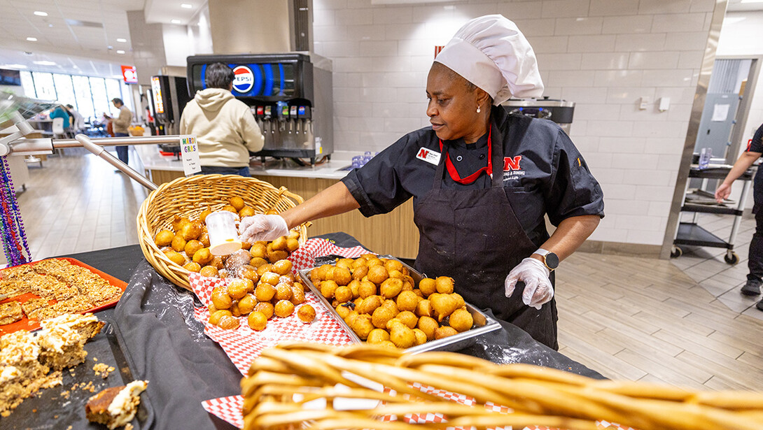 Hope Lifaefi, a Massengale Dining Hall Prep Chef, sets out more beignets and adds powdered sugar to them for the East Campus Mardi Gras feast.