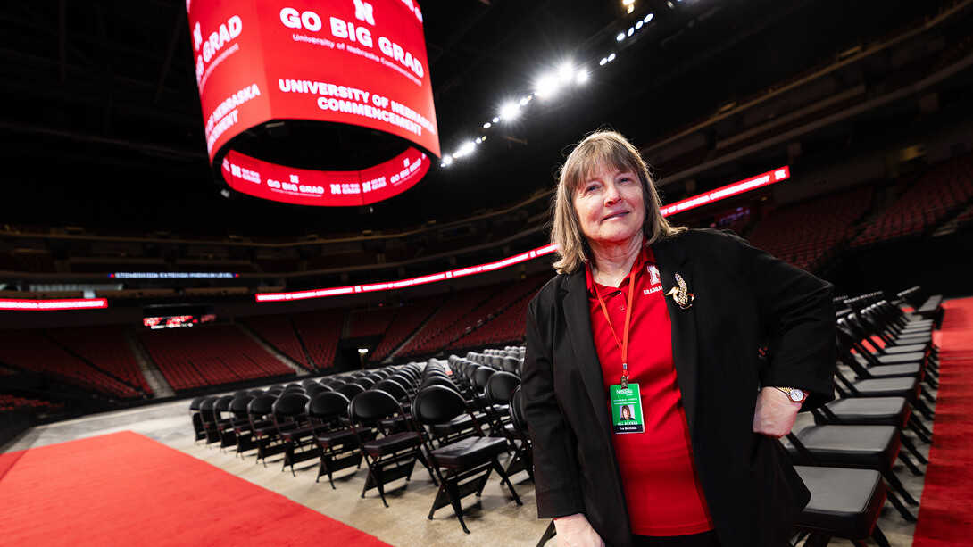 Eva Bachman, director of graduate student support and associate registrar, stands in Pinnacle Bank Arena as crews set up for the graduate commencement ceremony on May 7. For 20 years, Bachman has worked behind the scenes to get graduate students successfully across the stage. She is wearing a brooch from her grandmother, who bought Bachman's textbooks and supported her academic journey.