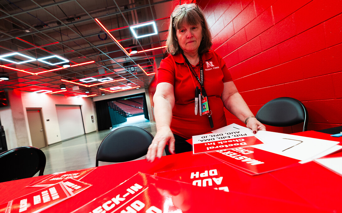 Eva Bachman, director of graduate student support and associate registrar, reaches for a sign directing students to check in with Graduate Studies to receive their name cards before commencement.