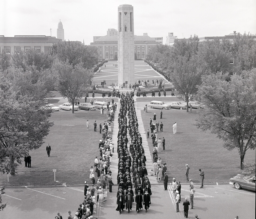 Nebraska graduates walk down the mall between Love Library and the Coliseum in this undated photo. Also pictured is Mueller Tower.