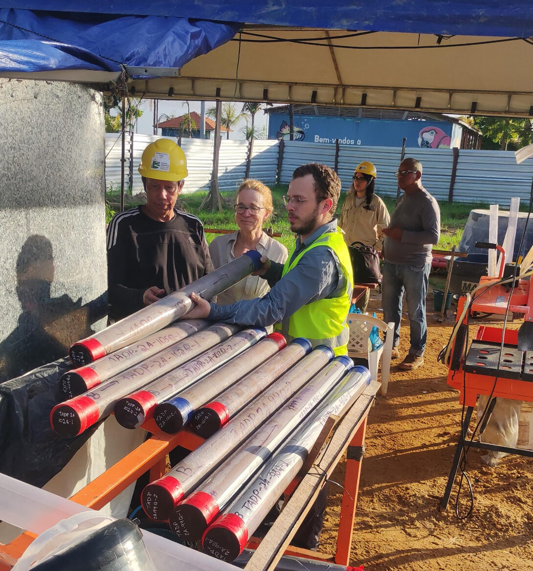 Three people handle cores of sediment at a drill site